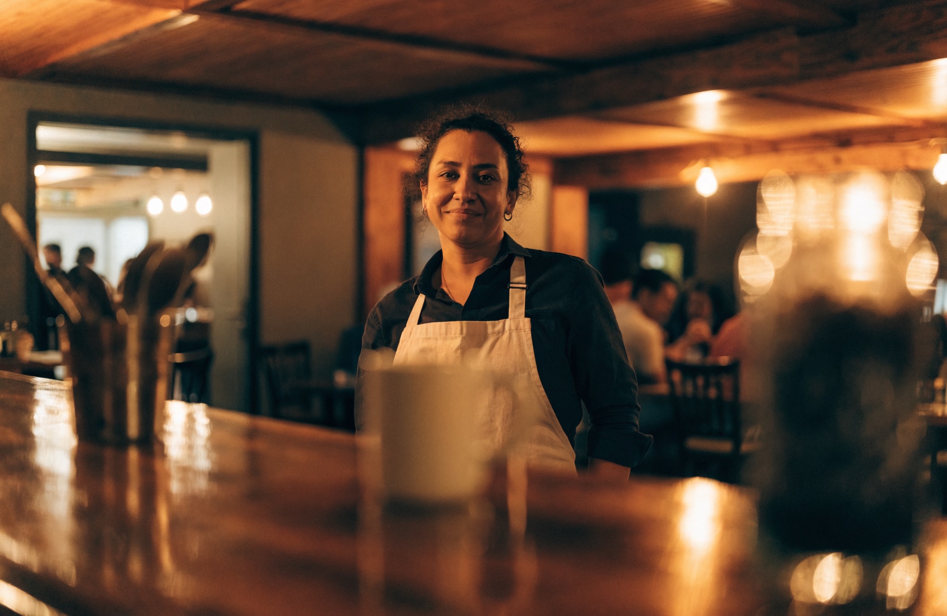 A bar and restaurant owner standing behind a warm, welcoming wooden bar